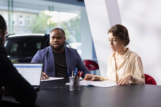 Customers in car dealership browsing automobiles catalog, checking features and pricing options before taking test drive. Clients comparing vehicle models before committing to investment photo