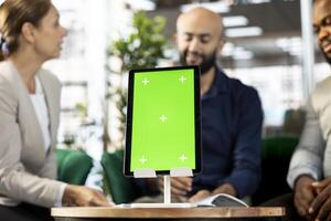 Focus on isolated screen tablet in front of businesspeople talking in startup company, looking at financial business documents. Close up of mockup device used by office clerks in blurry background photo