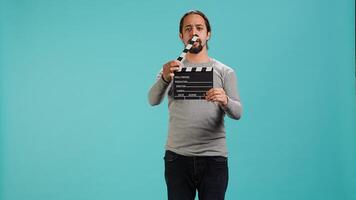 Movie director using clapper to signal actors beginning of scene recording, studio background. Film producer on set filming production, using clapperboard, camera A photo