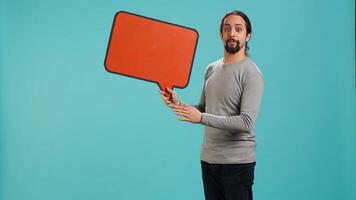Smiling man holding red speech bubble sign of empty copy space for message. Joyous person presenting thought bubble cardboard used as promotion concept, studio background, camera A photo