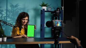Woman holding green screen tablet, talking about specifications, filming with professional camera. Internet show host presenting chroma key device features, recording with filming gear, camera B photo