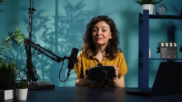 Happy tech content creator filming technology review of newly released VR glasses, unpacking them and presenting specs to fans. Jolly woman showing virtual reality headset to subscribers, camera B photo