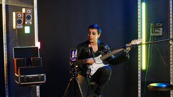 Musical instructor influencer creating content while playing guitar and singing alternative music, live audience online concert. Artist broadcasting her performance on streaming session. Camera B. photo