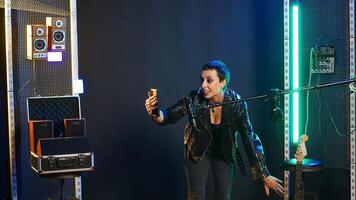 Rocker singer chatting on a call and showing the studio on a selfie camera, smartphone user recording her singing session. Cool edgy artist on live chat having a conversation. Camera B. photo