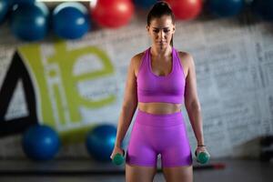 A focused and determined woman performs a strength building dumbbell workout at the gym, showcasing her athletic physique and dedication to fitness. photo