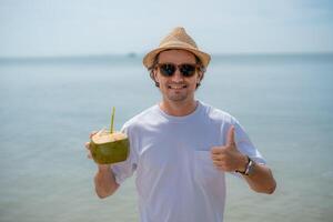 Man enjoying a coconut drink on a sunny beach with calm waters in the background photo