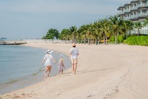 Family enjoys a sunny day walking along the calm beach with palm trees and water in the background photo