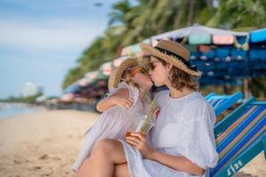 Mother and daughter enjoying a sunny day at the beach, sharing a sweet moment and refreshing drink while relaxing photo