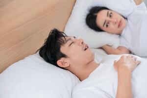 Couple in bed with one partner snoring while the other looks concerned during early morning hours photo
