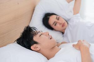 Couple in bed during morning hours, one partner sleeping while the other looks concerned photo