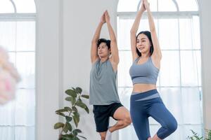 Yoga practitioners engaging in a balanced pose in a bright studio with large windows and plants in the background photo