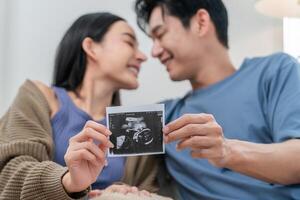 A happy couple sits resting on their laps, showcasing an ultrasound image with smiles. The warm atmosphere captures their excitement about expecting a baby. photo