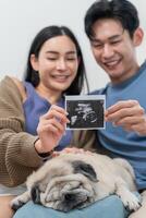 Excited couple shares ultrasound image while sitting on a couch with their sleeping dog photo