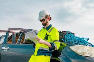 Construction worker reviews plans while standing next to vehicle on a job site in daylight photo