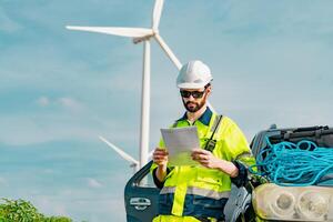 Worker reviewing documents near wind turbines on a sunny day while standing beside a vehicle photo