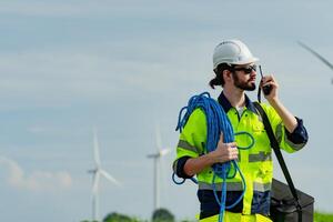 Worker in high visibility clothing communicating on walkie-talkie near wind turbines under a cloudy sky photo