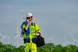 Construction worker in high visibility gear communicates on radio near wind turbines during the day photo