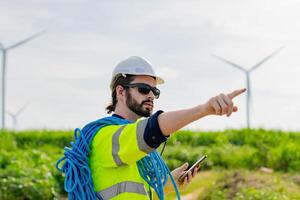 Worker directs team in renewable energy field while wearing safety gear and holding a smartphone photo