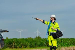 Professional technician conducts maintenance in a renewable energy field with wind turbines in the background photo