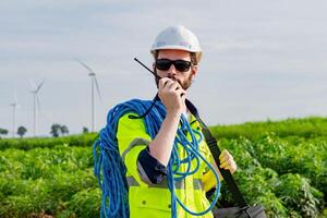 Worker communicates on radio while managing equipment near wind turbines in green field landscape photo
