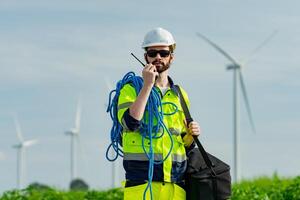 Worker in safety gear communicates while standing near wind turbines in a green field during the day photo