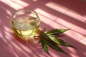 close-up of a glass jar with hemp oil surrounded by marijuana leaves on a pink surface photo