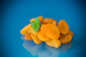 A handful of bright orange dried apricots with a sprig of mint on a blue background photo