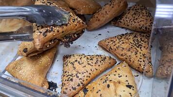 Tongs selecting freshly baked pastries with sesame seeds from bakery display video