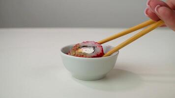 Hand skillfully dipping sushi roll into soy sauce with chopsticks on white surface video