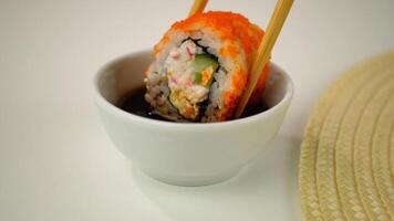 Closeup of vibrant sushi roll dip with chopsticks in soy sauce on elegant plate video