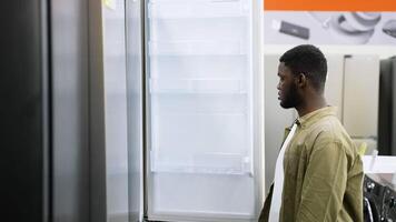 Man inspecting an empty refrigerator in appliance store video