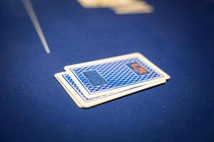 Two face down playing cards rest on a blue felt poker table with a geometric pattern. The blurred background suggests additional game elements. photo
