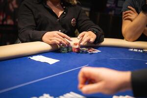 A poker game in progress with players seated around a blue felt table. Focus on hands stacking colorful chips, playing cards, and folded paper. photo