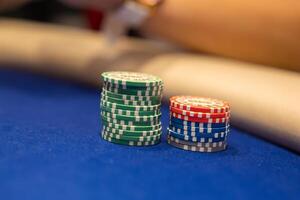 Poker chips in green, red, blue, and gray with white detailing are stacked on a blue felt table. A blurred arm suggests an active game in progress. photo