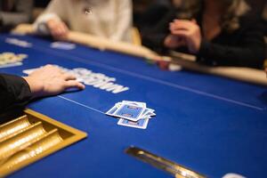 A poker game in progress on a blue felt table with visible branding, a gold card slot, chips, and hands reaching toward face down cards. photo