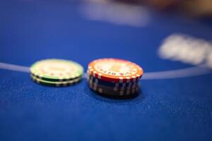 Close up view of poker chips in red, black, and green stacked on a blue felt table. Text and designs on the chips indicate denominations or branding. photo