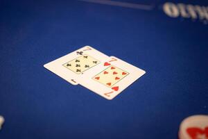 Two playing cards, the 7 of clubs and 7 of hearts, on a blue poker table with a partial logo and poker chip visible, suggesting a casino game. photo