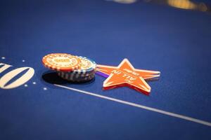 A blue felt poker table with multicolored chips, a red star shaped All In marker, and white markings, creating a professional casino setting. photo