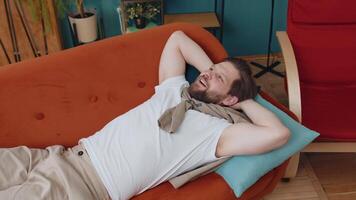 Tired young man lying down on comfortable couch, taking a rest, daytime nap relaxing falling asleep video