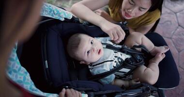 Handheld high angle view shot, Two young Asian women play with a little boy in a baby stroller outside a coffee shop. A relaxing atmosphere with a warm moment. video