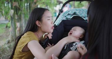 Handheld selective focus shot, Two young Asian women play with a little boy in a baby stroller outside a fee shop. A relaxing atmosphere with a warm moment video
