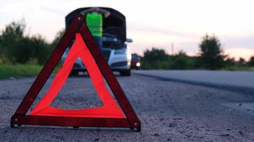 Unrecognizable sad driver in reflective vest holding head. Male driver standing near broken car with open up hood. Red triangle to warn other road users of car breakdown or engine failure stop at countryside highway. Emergency traffic situation video