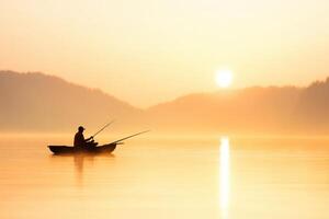 Silhouette of a person fishing from a small boat on a calm lake at sunrise with foggy mountains photo