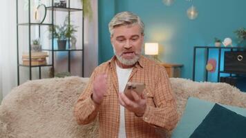 Mature man having phone argument on speaker, expressing stress and negative emotions on sofa at home video