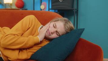 Teenager boy with toothache, holding cheek suffering unbearable pain grimacing lying on sofa at home video