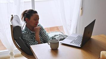 A young woman enjoying remote work from her comfortable home office setting. She sits with a laptop and coffee, exuding serenity and productivity in a bright, inviting room. photo