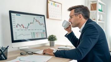 a man in a suit is sitting at a desk with a computer screen showing stock market graphs photo