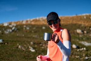 A female hiker enjoys a warm cup of tea while resting after a challenging mountain climb.A woman hiker takes a peaceful break, sipping tea and enjoying the view after a strenuous mountain climb photo