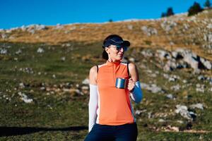 A female hiker enjoys a warm cup of tea while resting after a challenging mountain climb.A woman hiker takes a peaceful break, sipping tea and enjoying the view after a strenuous mountain climb photo