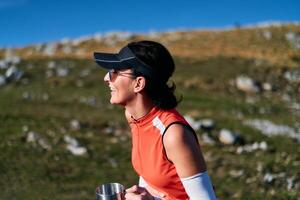 A female hiker enjoys a warm cup of tea while resting after a challenging mountain climb.A woman hiker takes a peaceful break, sipping tea and enjoying the view after a strenuous mountain climb photo